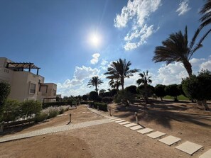 A residential area with a paved walkway, palm trees, and a building with a modern design. - Cyan Elegant 3BR Golf View Escape (Hurghada)