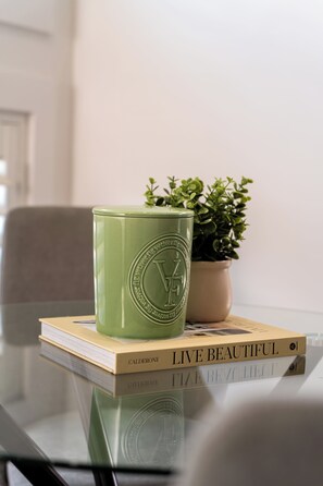 A green container with embossed text on a glass table, a book titled 'LIVE BEAUTIFUL' by Calderone, and a small potted plant. - A Dahlia by Esteem Retreats (Quakers Hill)