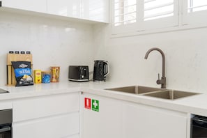 A modern kitchen with a stainless steel sink, a kettle, a toaster, and a fire extinguisher. - A Dahlia by Esteem Retreats (Quakers Hill)
