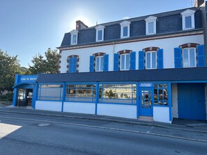 Um edifício de dois andares com uma padaria e café no andar térreo, com portadas azuis e fachada branca.