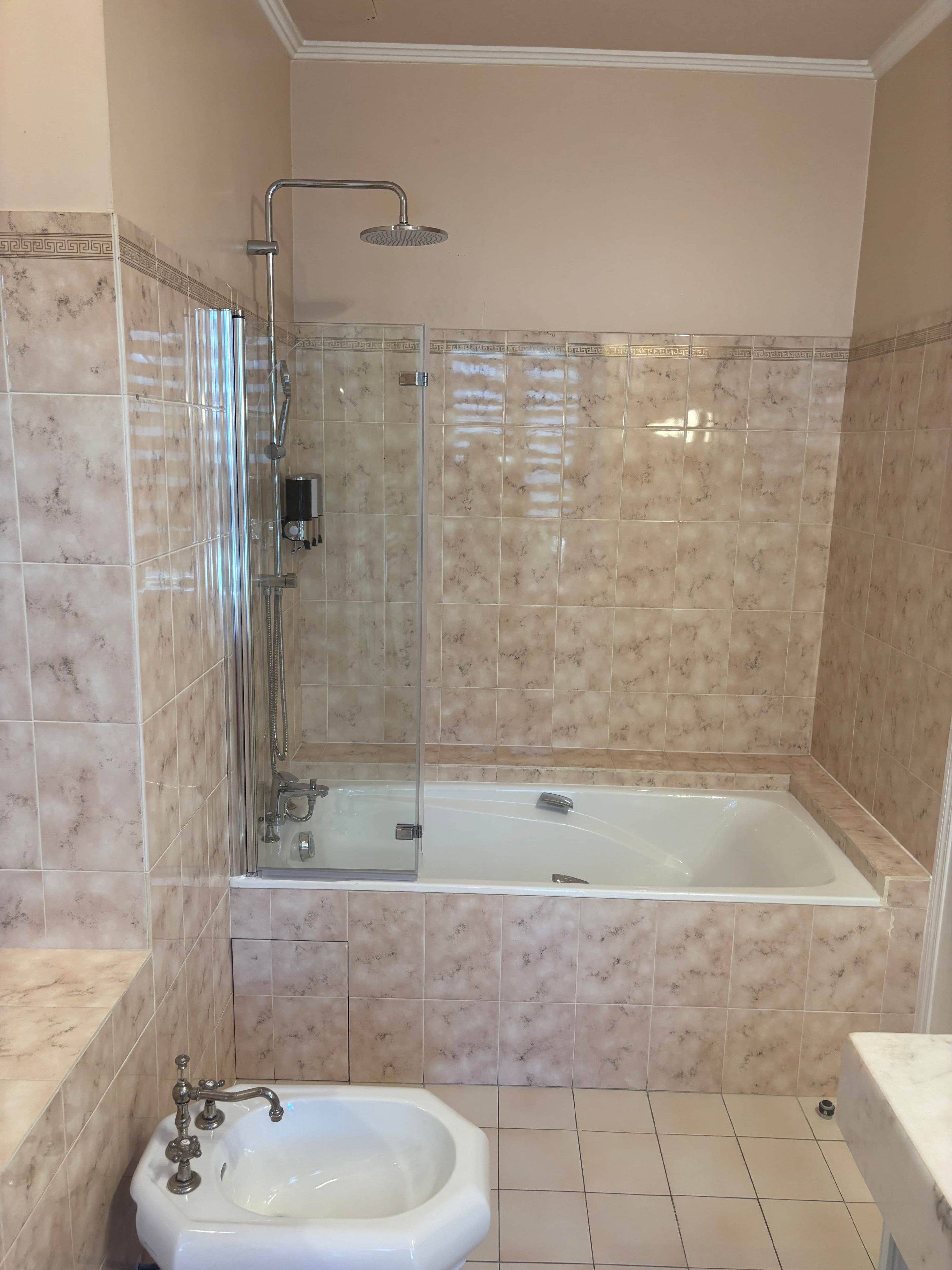 Een badkamer met een douche met glazen wand, een bad en een wastafel op een zuil.