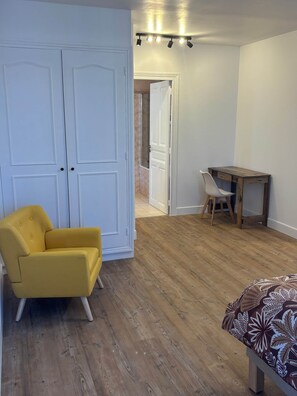 Una habitación con piso de madera, un sillón amarillo, una mesita de madera y un armario blanco.