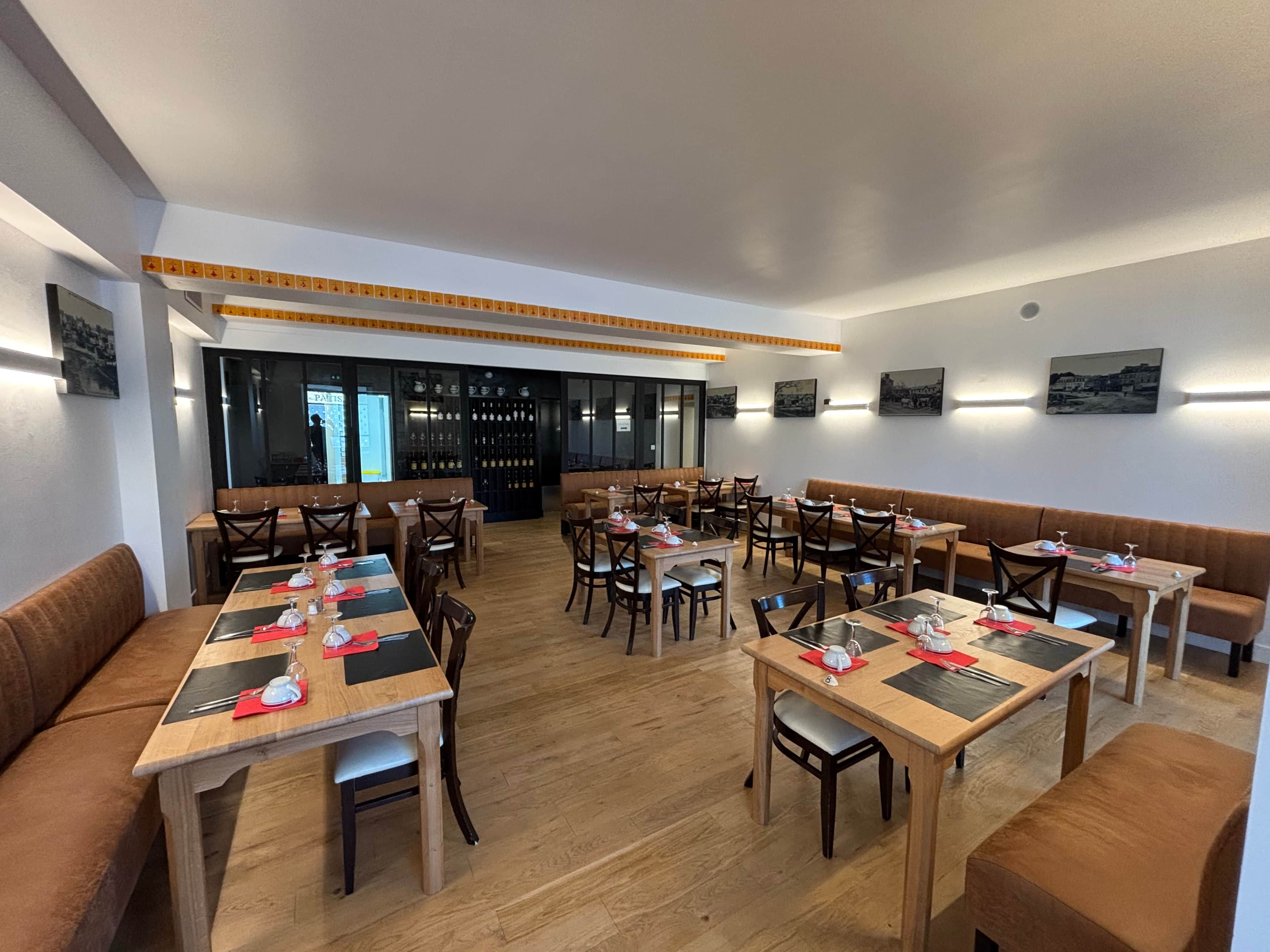 En restaurant med flere borde og siddepladser, trægulv og et vinskab i baggrunden.