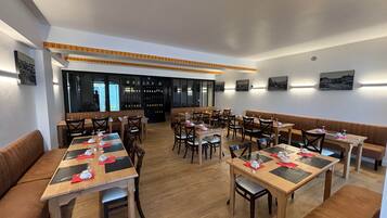 En restaurant med flere borde og siddepladser, trægulv og et vinskab i baggrunden.