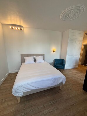A bedroom with a large bed, a blue armchair, and a wardrobe. - TYYANN 8: A 26-square-meter studio equipped with a kitchenette and a bathroom (Plancoët)