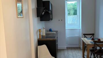 Een compacte keuken met een inbouwfornuis, een eethoek met een tafel en stoelen, en een raam dat voor daglicht zorgt.