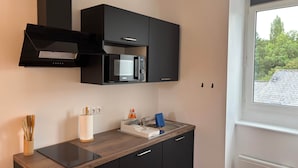 A modern kitchen with a microwave, cabinets, and a window with a view of greenery. - TYYANN 9: A 30-square-meter studio equipped with a kitchenette and a bathroom (Plancoët)