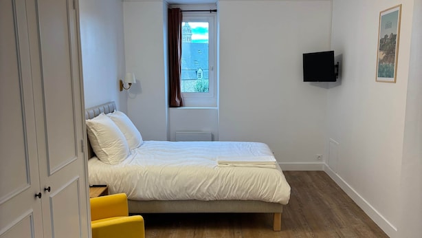 A bedroom with a bed, a window, a television, and a door. - TYYANN 9: A 30-square-meter studio equipped with a kitchenette and a bathroom (Plancoët)