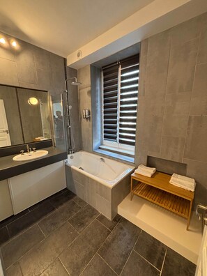 A modern bathroom with a bathtub, a sink, a mirror, and a window with blinds. - TYYANN 2: A 26-square-meter studio with a kitchenette and a bathroom (Plancoët)