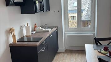 Une cuisine moderne avec des meubles de rangement noirs, une poubelle en acier inoxydable et un coin repas comprenant une table et des chaises.
