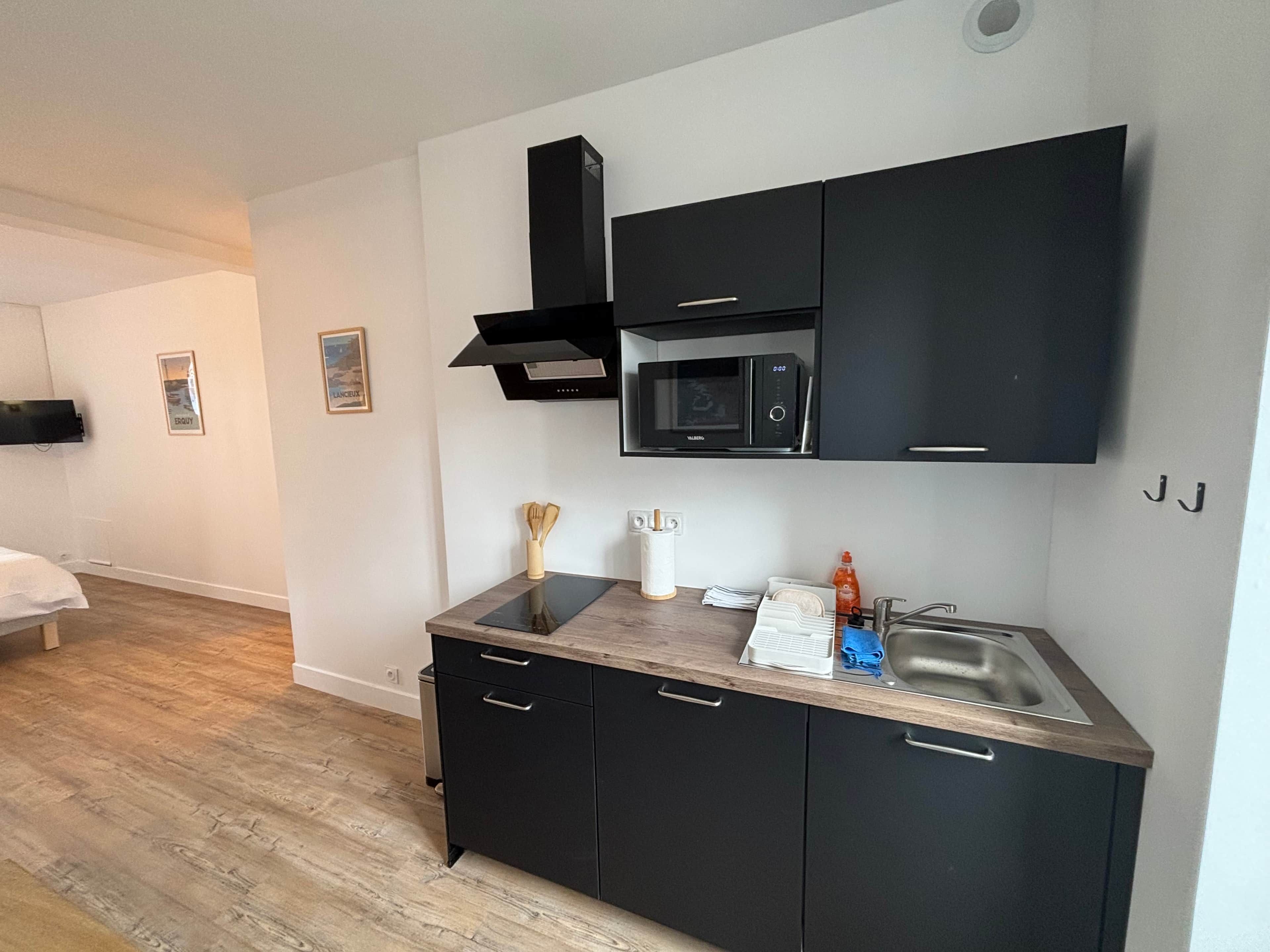 A modern kitchen with black cabinets, a microwave, and a stainless steel sink.