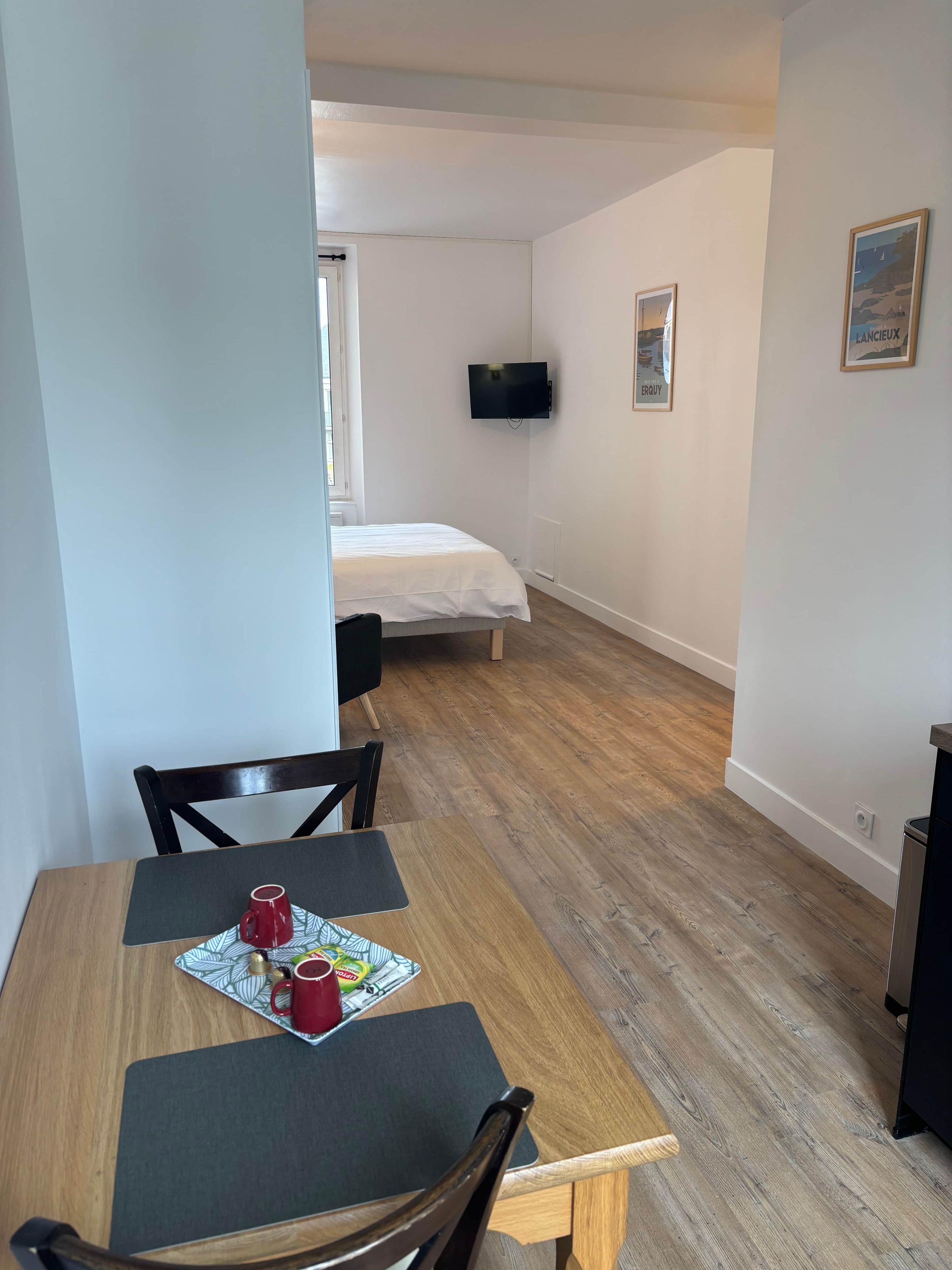 Une chambre de taille modeste, équipée d’un lit, d’un téléviseur fixé au mur et d’un coin repas avec une table et des chaises.