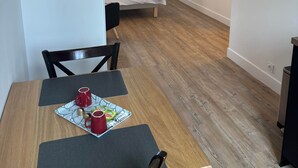 Quarto compacto com cama, televisão na parede e área de refeições com mesa e cadeiras.