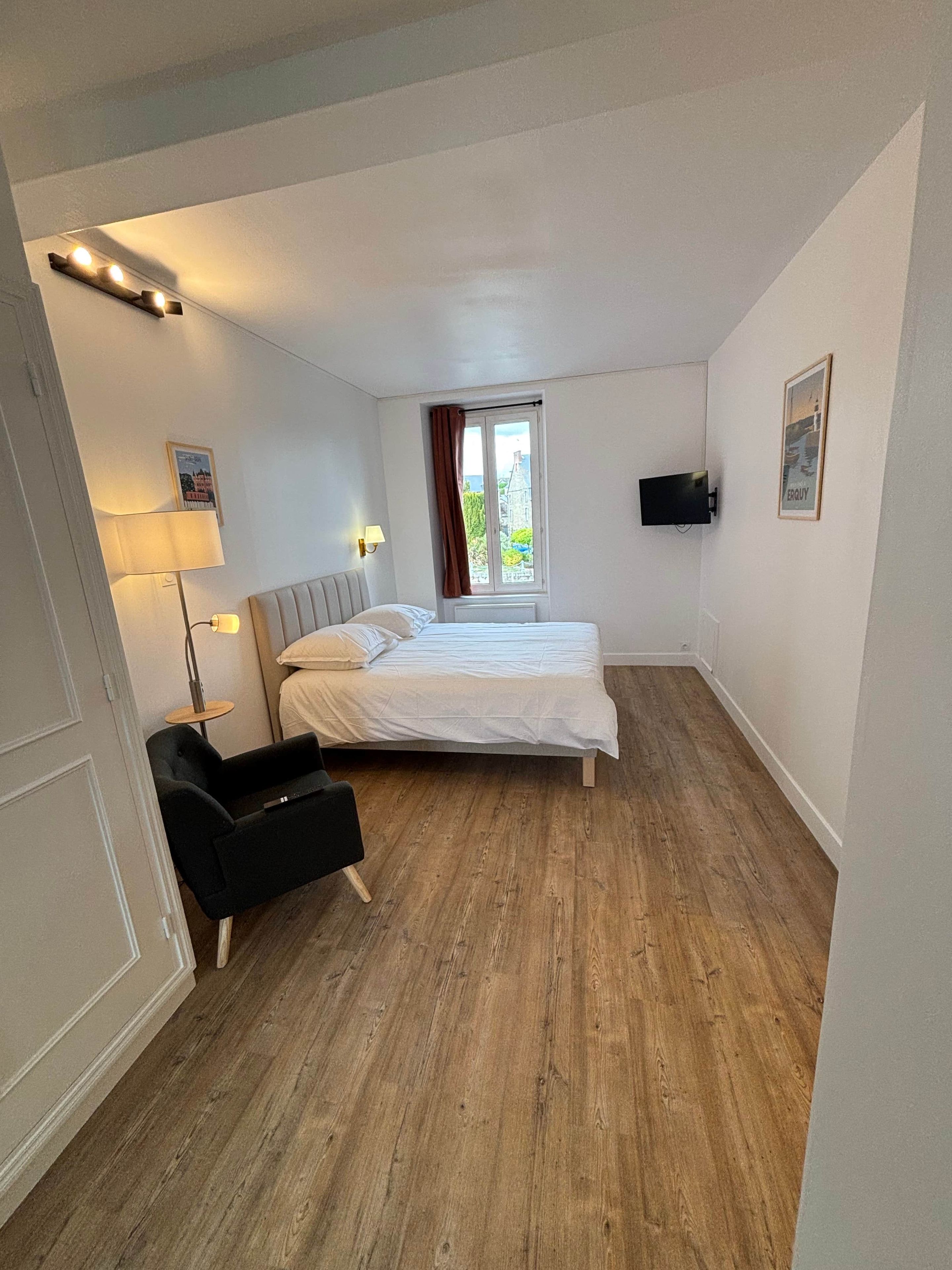 Une chambre à coucher comprenant un lit, un bureau, une chaise, une fenêtre avec des rideaux et un téléviseur fixé au mur.