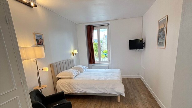 Quarto com cama, escrivaninha, cadeira, janela com cortinas e televisão na parede.