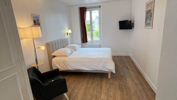 Une chambre à coucher comprenant un lit, un bureau, une chaise, une fenêtre avec des rideaux et un téléviseur fixé au mur.
