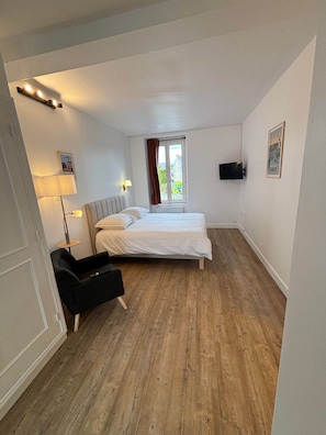 Een slaapkamer met een bed, een bureau, een stoel, een raam met gordijnen en een tv aan de muur.