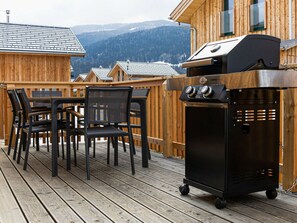 A wooden deck with a grill, chairs, and a view of mountains. - Cabin With 1 Bedroom (Sankt Georgen am Kreischberg)