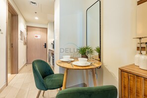 Un couloir avec une porte en bois, un fauteuil recouvert d’un tissu vert, une petite table ronde avec un bol et un verre à vin, et un miroir accroché au mur.