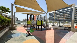 Un espace de jeux extérieur avec un toboggan et une structure d’escalade, entouré de bâtiments.