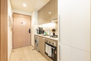 A compact kitchen with a washing machine, a stove, and a microwave. - Studio w/ Community View,Near Meydan Golf Club, Approx 15Min Drive to Downtown (Dubai)