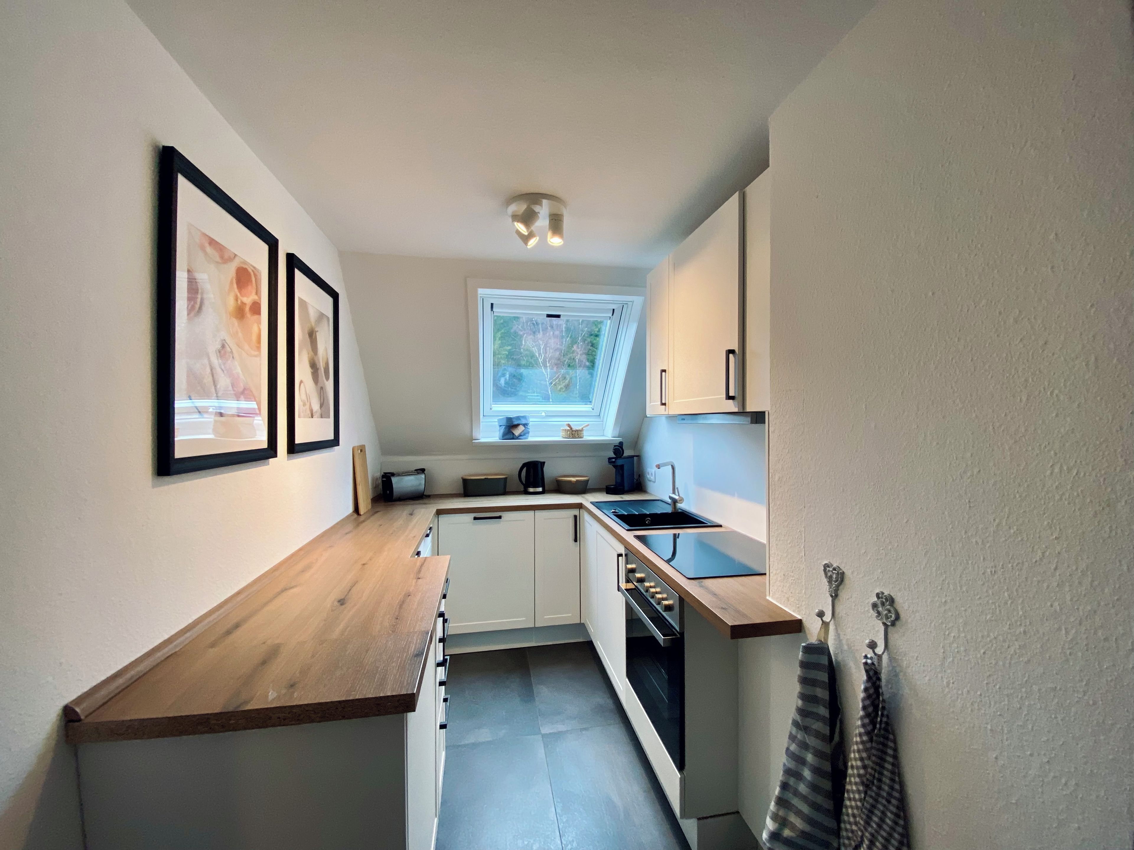 A compact kitchen with white cabinets, a wooden countertop, a window, and a ceiling light fixture.