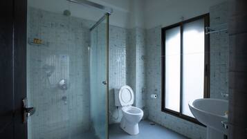 A modern bathroom with a glass shower enclosure, a white toilet, and a large window providing natural light.