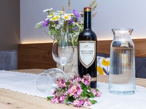 Eine Flasche Malvasija Istarska Wein, eine Krug und eine Vase mit Blumen auf einem Holztisch.
