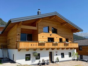 Ein zweistöckiges Holzhaus mit Balkon, Schornstein und einer Steinterrasse.