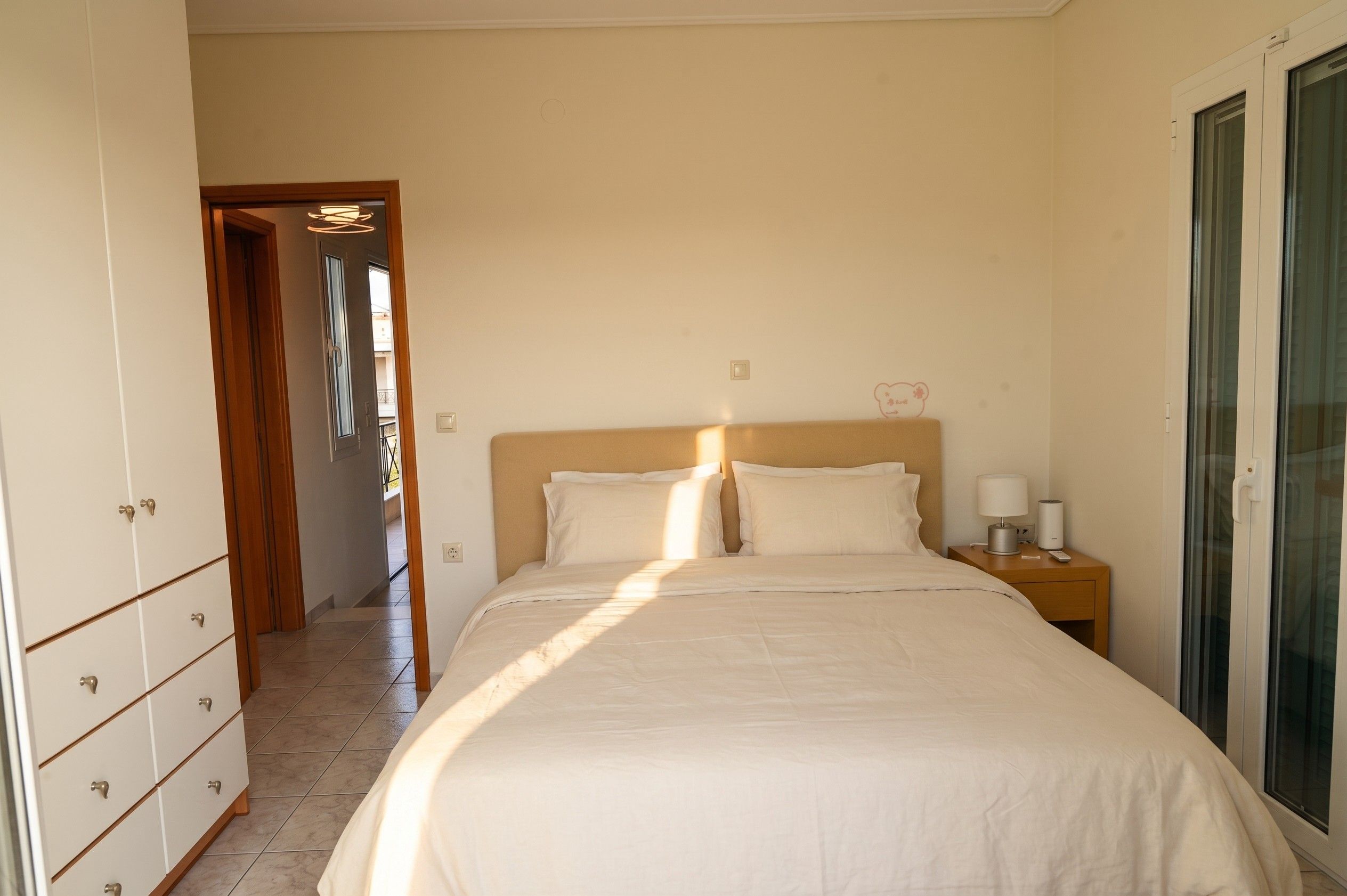 A bedroom with a bed, a nightstand, a wardrobe, and a door leading to another room.