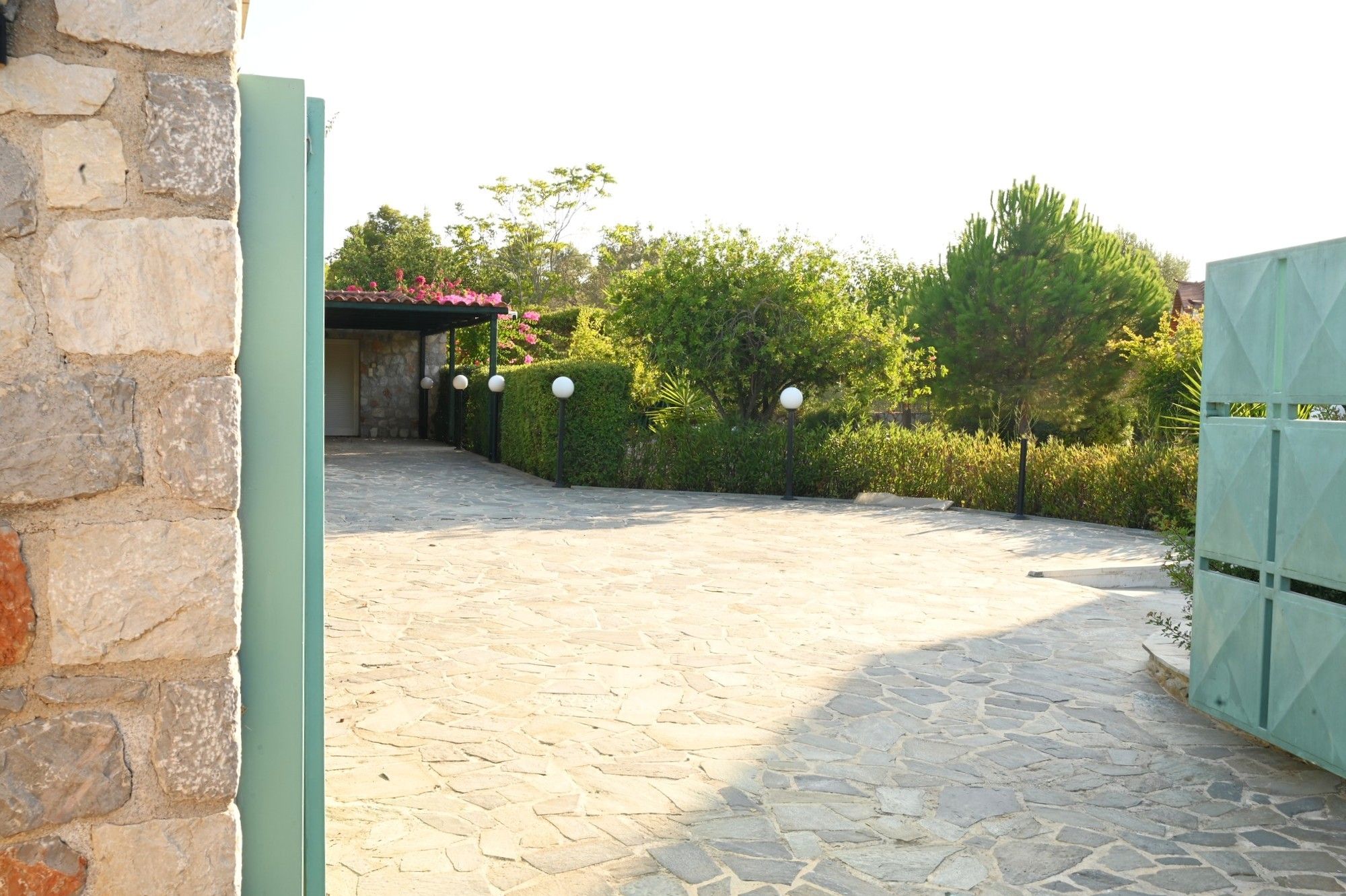 Un patio empedrado con suelo de piedra, un portón verde y una pared de piedra a la izquierda.