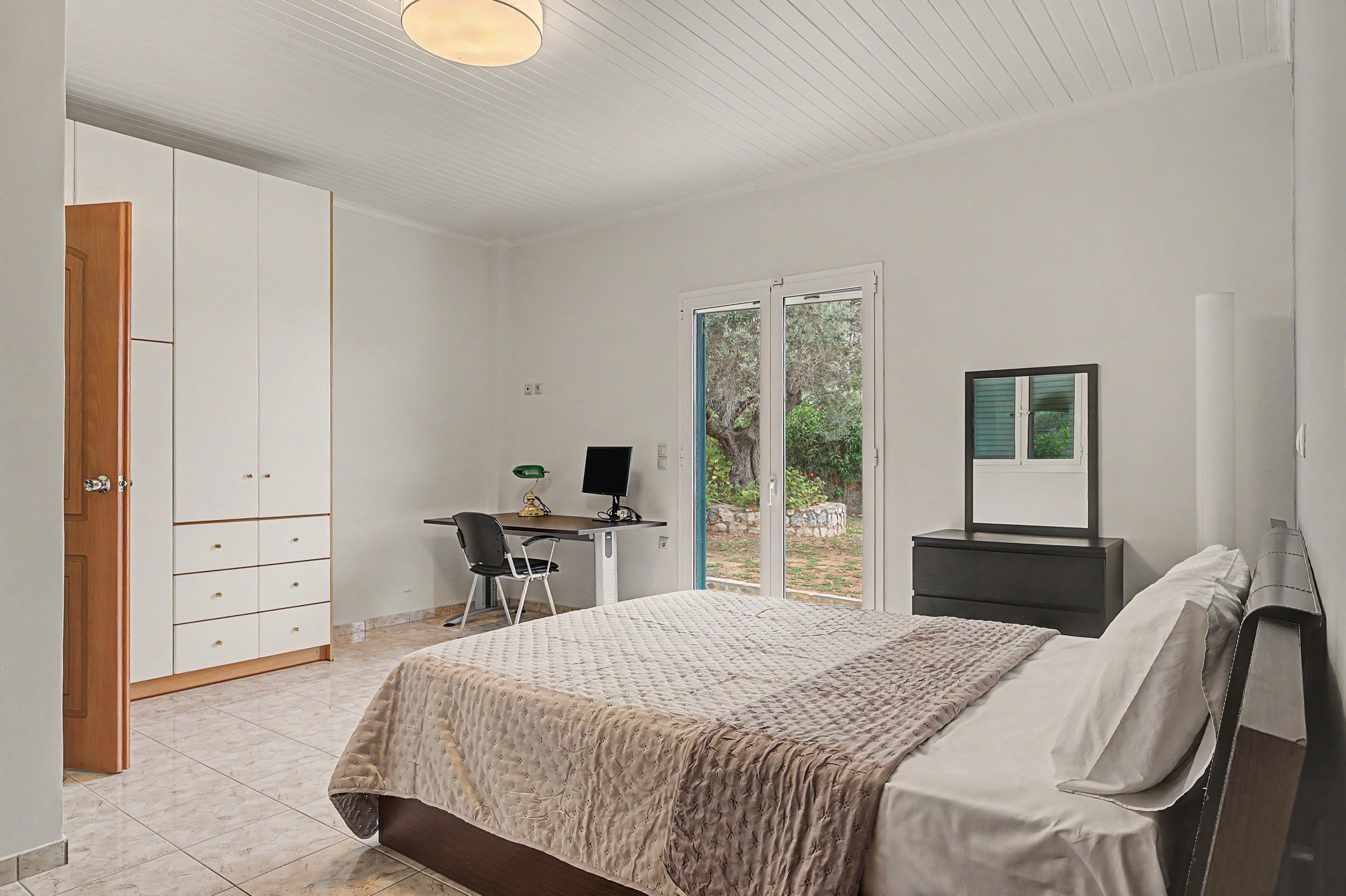A bedroom with a bed, a desk, a chair, a wardrobe, and a window.