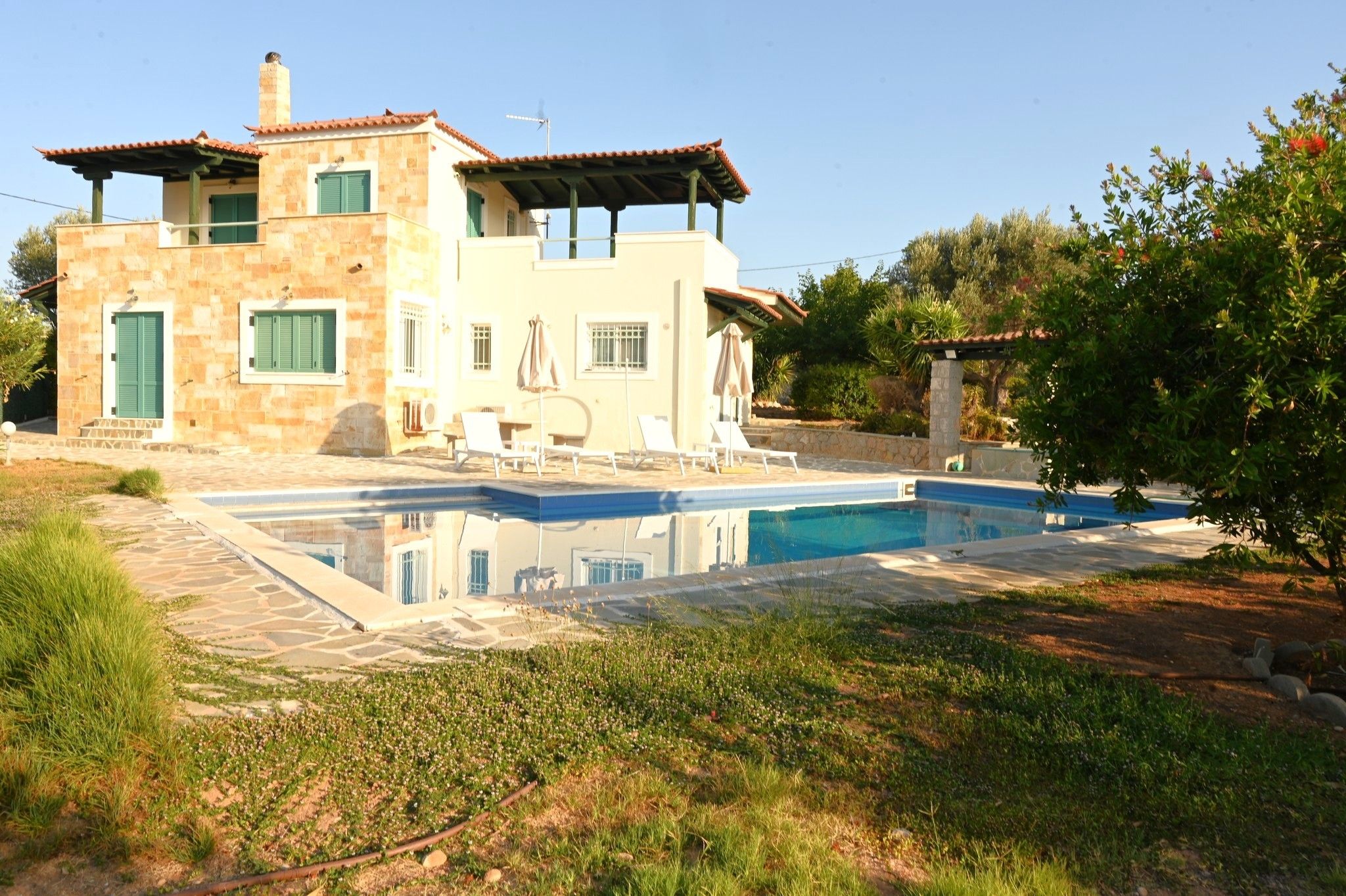 A two-story house with a swimming pool, outdoor seating, and a garden.