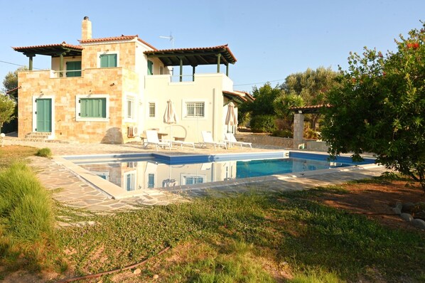 A two-story house with a swimming pool, outdoor seating, and a garden.