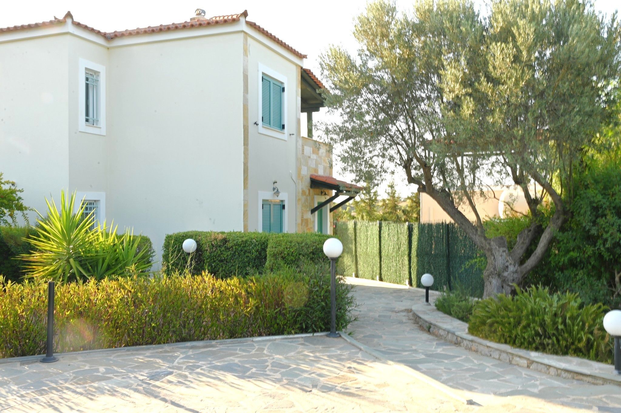 A two-story building with a paved entrance and a well-maintained garden with hedges and a tree.