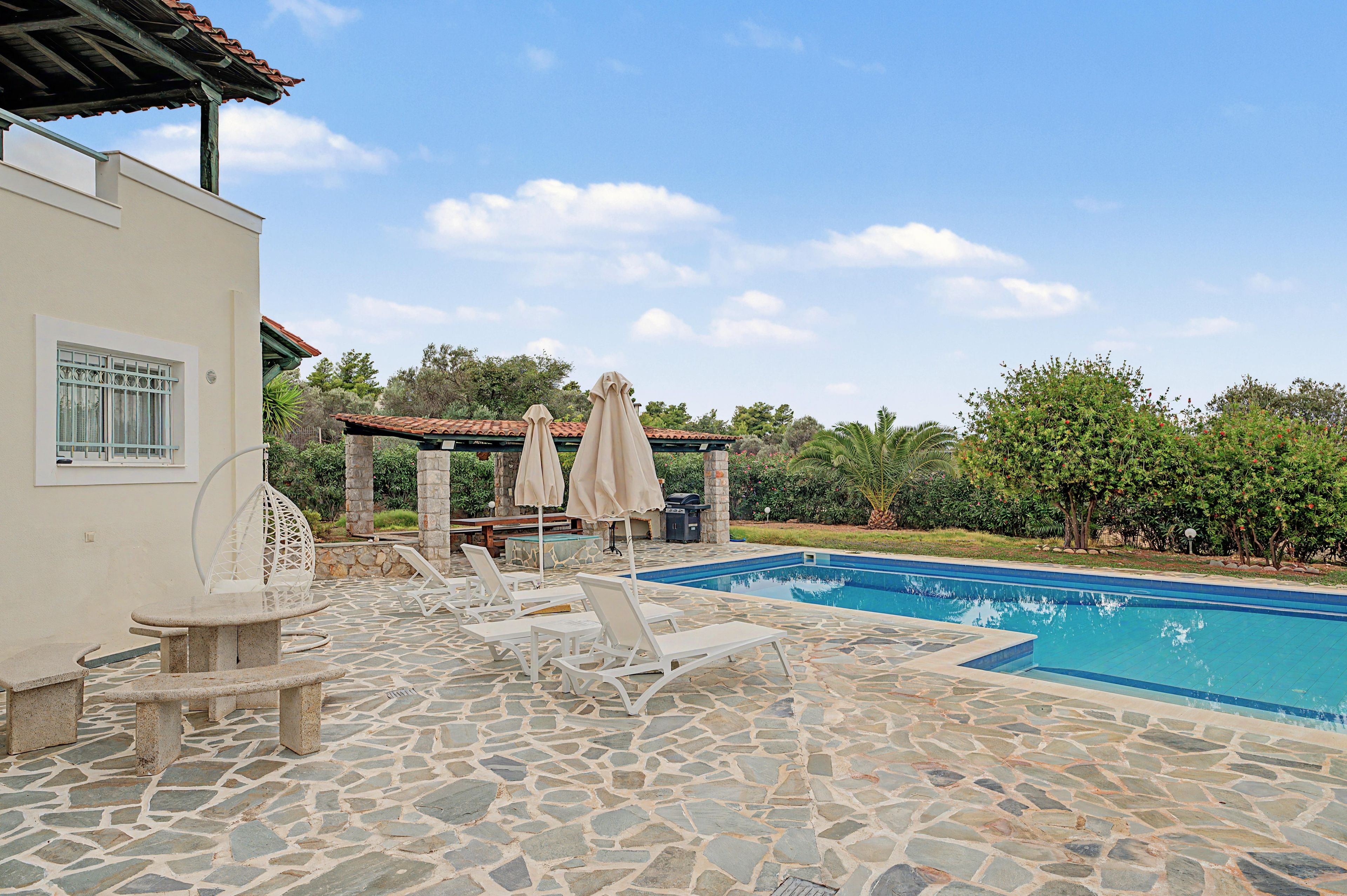 A swimming pool with lounge chairs and umbrellas, surrounded by stone tiles and greenery.