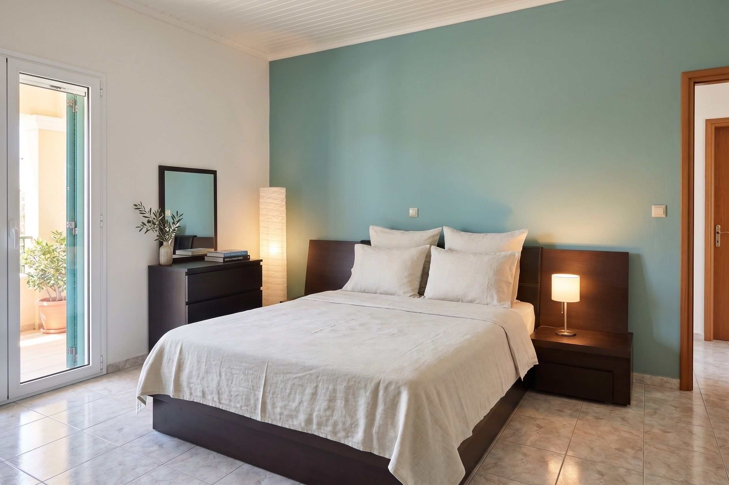 A bedroom with a bed, bedside tables, a nightstand, a lamp, a mirror, and a potted plant.
