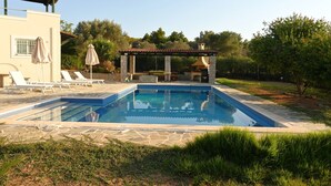 Ein rechteckiger Swimmingpool mit einer Steindeckplatte, umgeben von einer Terrasse mit Liegestühlen und Sonnenschirmen.