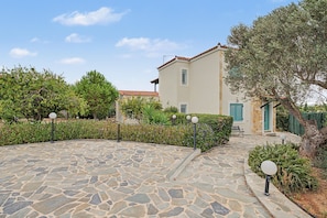 A stone-paved courtyard leading to a building with a tiled roof and a green door. - Welcome to Villa Almira: Detached 3-Bedroom Retreat with Private Pool (Κρανίδι)
