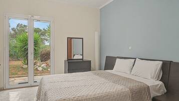 A bedroom with a bed, a nightstand, a mirror, and a sliding glass door leading to a garden.