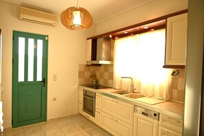A compact kitchen with a green door, a built-in oven, a sink, and a window with curtains. - Welcome to Villa Almira: Detached 3-Bedroom Retreat with Private Pool (Κρανίδι)