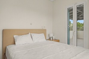 A bedroom with a bed, a nightstand, a lamp, and a sliding glass door to a balcony. - Welcome to Villa Almira: Detached 3-Bedroom Retreat with Private Pool (Κρανίδι)