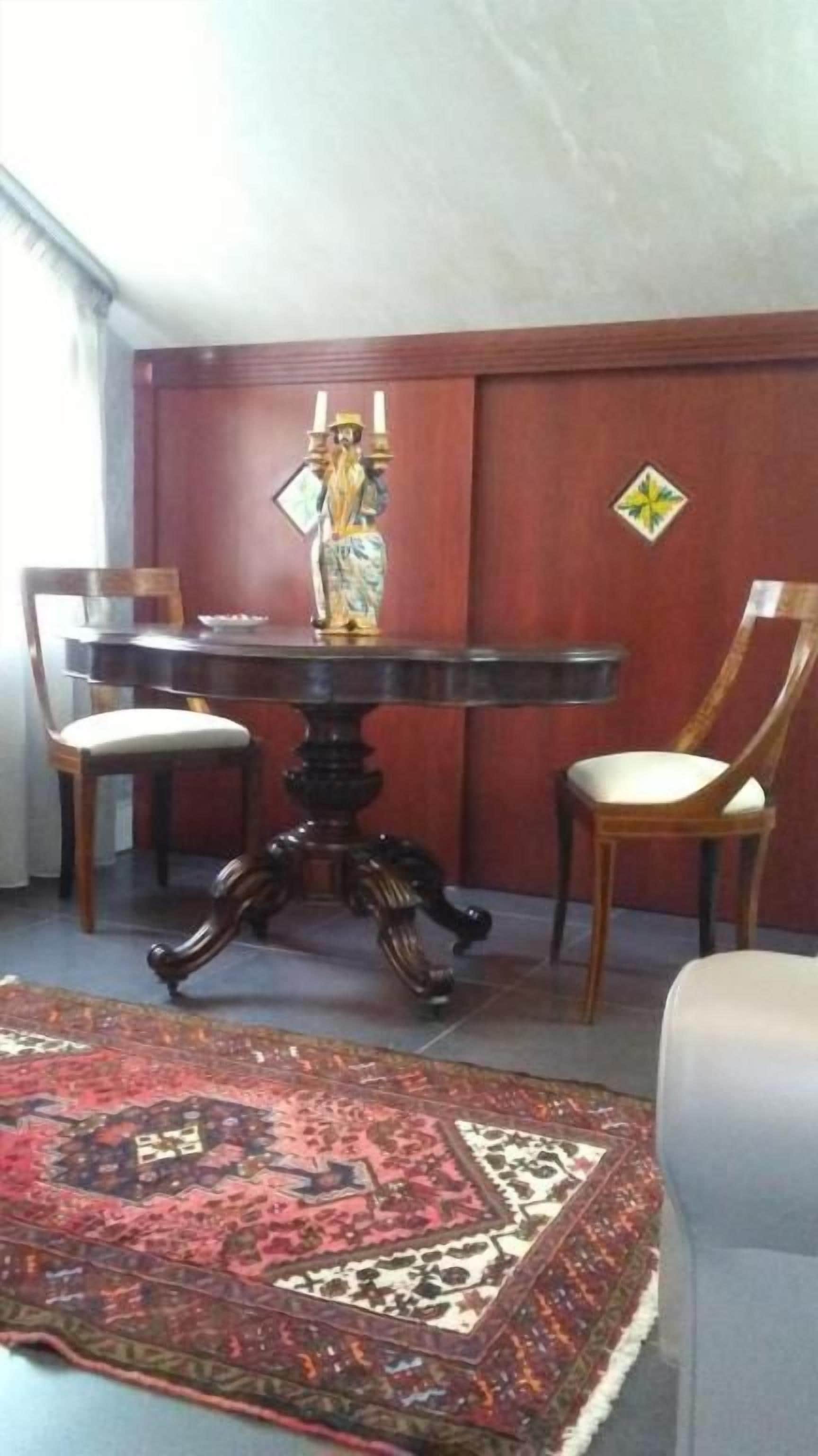 Zona pranzo con tavolo rotondo, due sedie, un vaso decorativo e un tappeto fantasia.