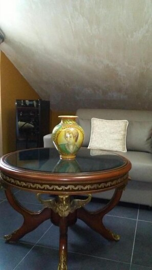 A round table with a vase and a cushion on a sofa in a room with a sloped ceiling. - Animosa Suite (Castiglione di Sicilia)
