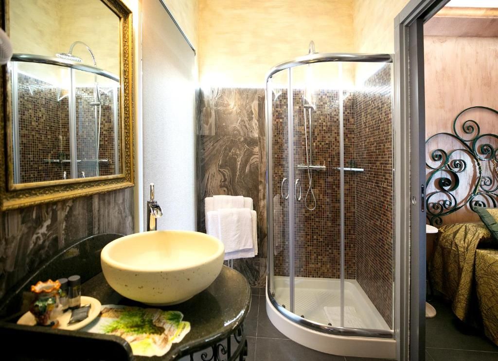 Un baño con un lavamanos redondo, cabina de ducha con mampara de vidrio y un espejo con marco decorativo.