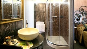 A bathroom with a round sink, a glass shower enclosure, and a mirror with a decorative frame. - Animosa Suite (Castiglione di Sicilia)