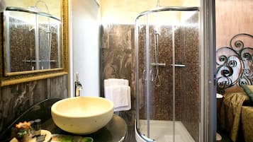 Un baño con un lavamanos redondo, cabina de ducha con mampara de vidrio y un espejo con marco decorativo.