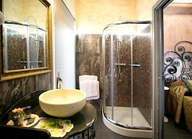 A bathroom with a round sink, a glass shower enclosure, and a mirror with a decorative frame.