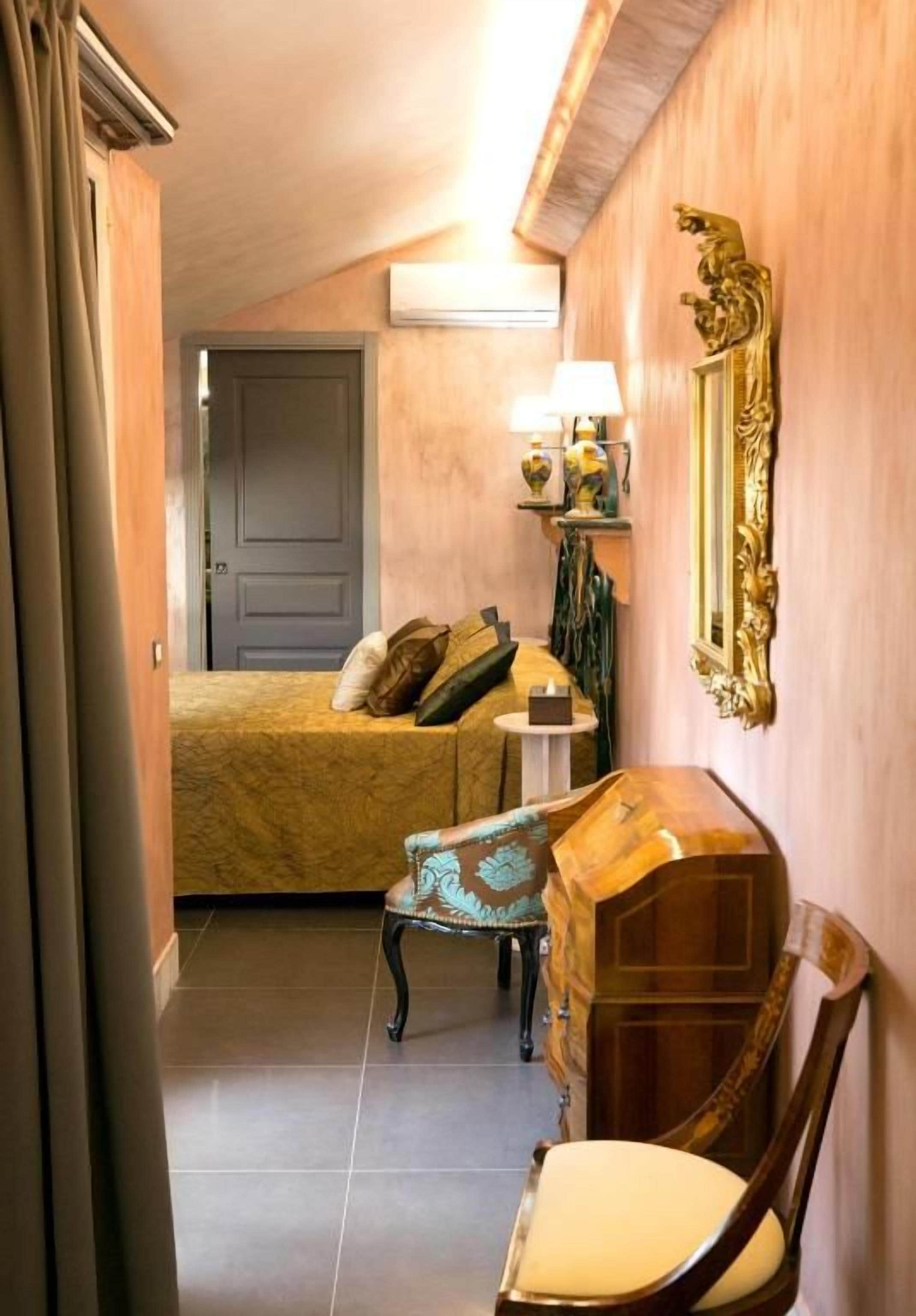 Une chambre d’hôtel avec un lit, une chaise, une petite table avec une lampe et un miroir décoratif.