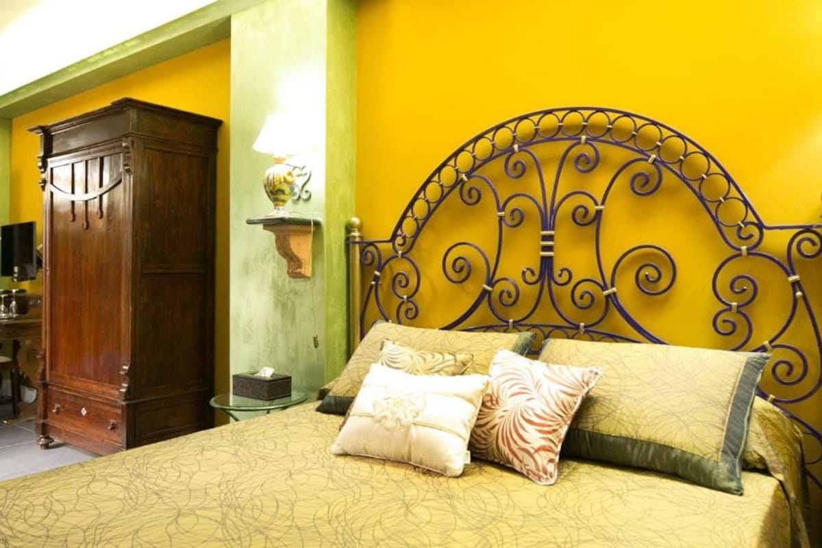 Uma cama com cabeceira de metal, guarda-roupa de madeira e mesa de cabeceira com abajur.